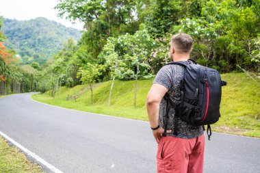Tayland ormanyolunda bir sırt çantası ile bir gezgin genç adam ile Yakışıklı tropikal orman. Bir adam tropik bir yolda yürür ve doğanın manzarasına sahiptir