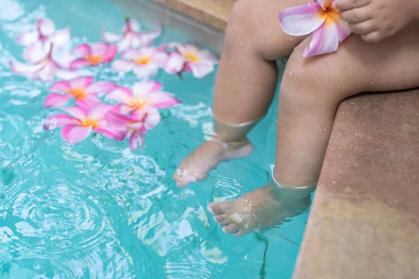 スイミングプールの赤ちゃんの足。熱帯の花フランジパニプルメリア、水に浮かぶリーラワディー。スパプール。平和と静けさスパコンセプト. — ストック写真