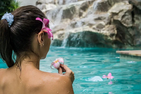female in a swimming pool. Tropical flowers Frangipani Plumeria, Leelawadee floating in the water. Spa pool. Peace and tranquility. Spa concept.