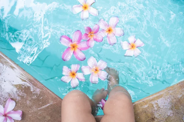 Baby Feet w basenie. Tropikalne kwiaty Frangipani Plumeria, Leelawadee pływających w wodzie. Basen spa. Spokój i cisza. Koncepcja Spa. — Zdjęcie stockowe