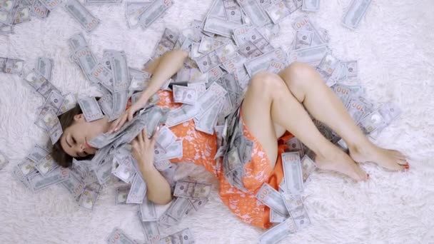 Το κορίτσι κείτεται σε λευκό κρεβάτι με πολλά λεφτά. Το κορίτσι απολαμβάνει πολλά λεφτά. αργή κίνηση. Τεράστιος πλούτος χρημάτων — Αρχείο Βίντεο