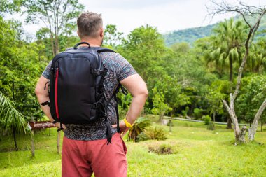 Tayland ormanyolunda bir sırt çantası ile bir gezgin genç adam ile Yakışıklı tropikal orman. Bir adam tropik bir yolda yürür ve doğanın manzarasına sahiptir