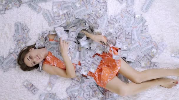 Spousta bankovek létá vzduchem na dívku ležící na bílé posteli v pomalém pohybu. Obrovské bohatství peněz — Stock video