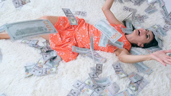 Много банкнот летит в воздухе на девочке, лежащей на белой кровати в замедленной съемке. Огромное богатство денег — стоковое фото