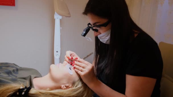 Молодая женщина проходит процедуру наращивания ресниц в салоне красоты, крупным планом — стоковое видео