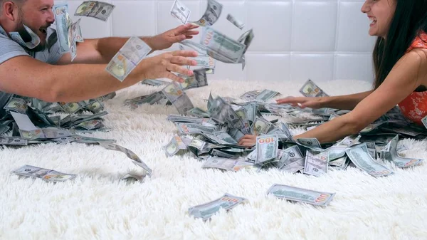 Female and male throw at each other a lot of banknotes of dollars on the bed, slow motion, top view — Stock Photo, Image