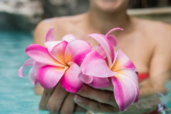 Woman holds flowers in a swimming pool. Tropical flowers Frangipani Plumeria, Leelawadee floating in the water. Spa pool. Peace and tranquility. Spa concept.