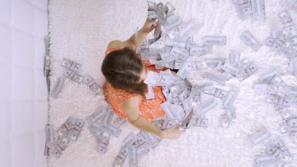 A beautiful girl enjoys tremendous wealth. female sorting out a lot of banknotes on a white bed, throws up money, slow motion, top view — Stock Video