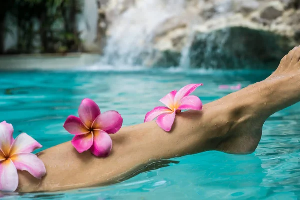 Woman Legs Beauty, Female Smooth Body, Foot Care, Hair Care. Beauty concept of woman legs, female smooth body, female foot in a pool with frangipani colors. Spa concept