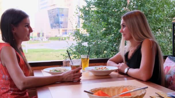 Zwei glückliche schöne Mädchen haben Spaß in einem Café an einem sonnigen Sommertag. — Stockvideo