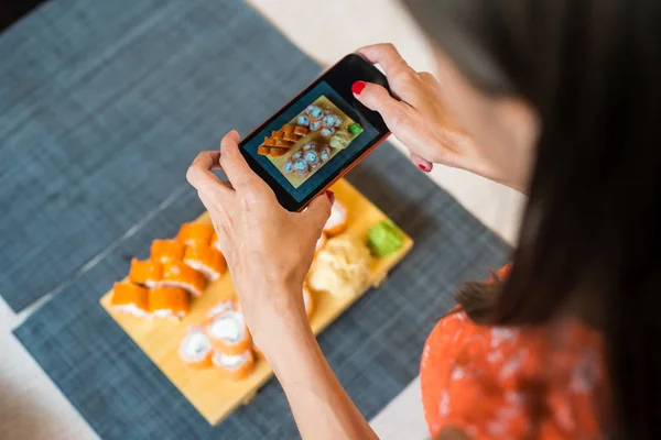 Girl takes pictures of sushi on phone. A girl takes pictures of sushi on the phone that lie on a black wooden table.