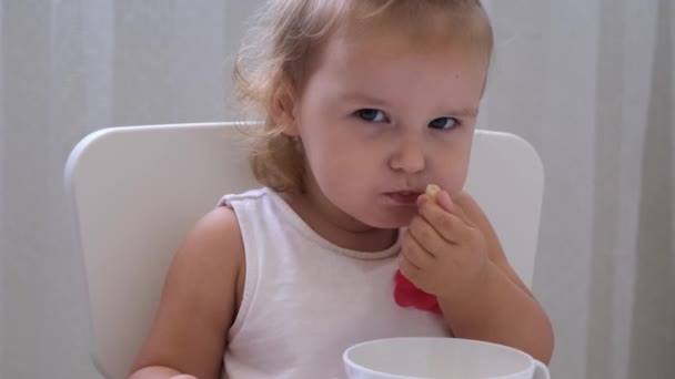 Ragazza neonata che mangia cibo per bambini a un piccolo tavolo per bambini su uno sfondo bianco. Nutrizione e alimentazione dei bambini . — Video Stock