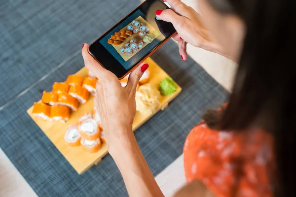 Girl takes pictures of sushi on phone. A girl takes pictures of sushi on the phone that lie on a black wooden table.