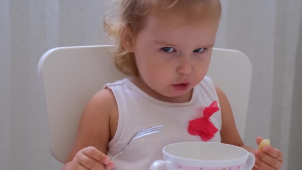 Ragazza neonata che mangia cibo per bambini a un piccolo tavolo per bambini su uno sfondo bianco. Nutrizione e alimentazione dei bambini . — Video Stock