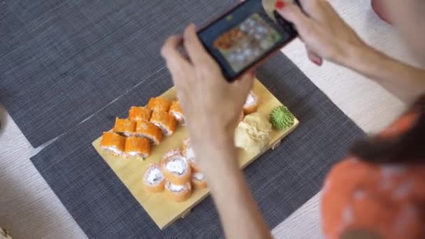 Chica toma fotos de sushi en el teléfono. Una chica toma fotos de sushi en el teléfono que se encuentran en una mesa de madera negro . — Vídeo de stock