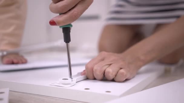 Twarde ręce zbierać pudełko, zbliżenie. Kobieta jest montaż białą drewnianą szafkę za pomocą śrubokręta. — Wideo stockowe
