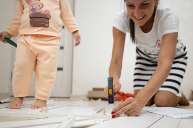 Anne ve kızı bir kutu toplar. Bir kadın tornavida kullanarak beyaz ahşap bir dolap montajı olduğunu.