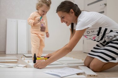 Anne ve kızı bir kutu toplar. Bir kadın tornavida kullanarak beyaz ahşap bir dolap montajı olduğunu.