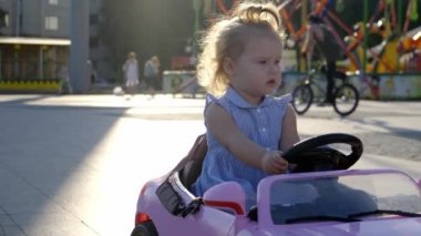 Mavi elbiseli küçük kız parkta pembe bir bebek arabasına biniyor. Mutlu çocukluk konsepti. Araba kullanan yetişkin bir kadının karikatürü.