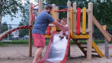 Baba ve kızı oyun alanında oynamak, bir adam bir çocuk slayt aşağı hareket eden bir kızı yakalar.