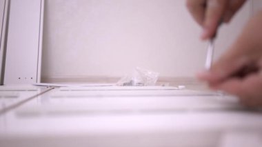 Sert eller kutu toplar, yakın çekim. Bir kadın tornavida kullanarak beyaz ahşap bir dolap montajı olduğunu.