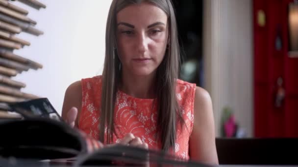 Schattige vrouw in een café met een menu in haar handen, een vrouw kiest eten en drinken op het menu om een bestelling te maken. — Stockvideo