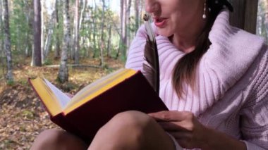 sonbahar ormanında kız, bir kitap okur, bir kadın sonbahar ormanında bir ağacın yanında oturur ve elinde bir kitap tutar