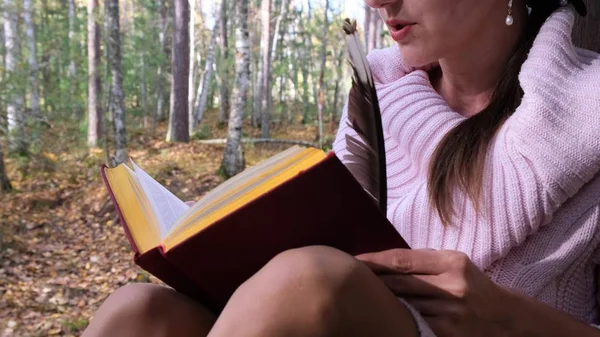 Primer plano de una niña en el bosque de otoño, una mano femenina escribe con un bolígrafo en un libro. Una mujer se sienta cerca de un árbol en el bosque de otoño y sostiene un libro en sus manos . —  Fotos de Stock