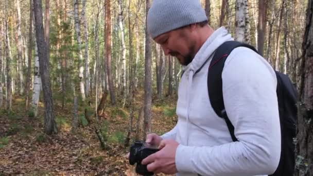 Человек держит камеру, фотографируя осеннюю природу на фоне пожелтевшего парка . — стоковое видео