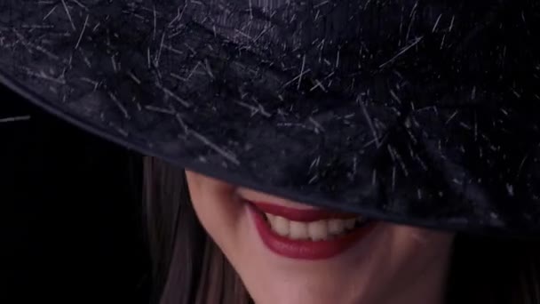 赤い唇と帽子の黒い魔女の衣装を着た美しい若いセクシーな女性は、カメラを見て笑っています。閉鎖 — ストック動画