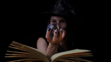 Siyah cadı kostümlü ve şapkalı güzel seksi kadın elinde şeffaf sihirli bir top tutuyor ve büyülüyor. Yakın plan. Cadılar Bayramı partisi.