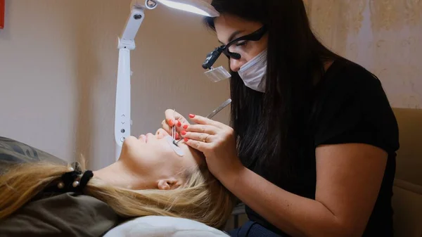 Olho de mulher com pestanas longas. Extensão das pestanas. Lashes, close up, foco selecionado. Colando pestanas artificiais com pinças. Esteticista em lupa óculos executa pequeno trabalho laborioso . — Fotografia de Stock