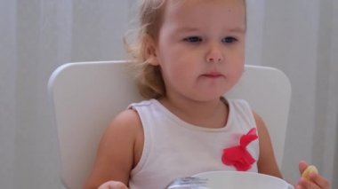 Bebek kız beyaz bir arka plan üzerinde küçük bir çocuk masasında bebek maması yiyor. Çocukların beslenmesi ve beslenmesi.