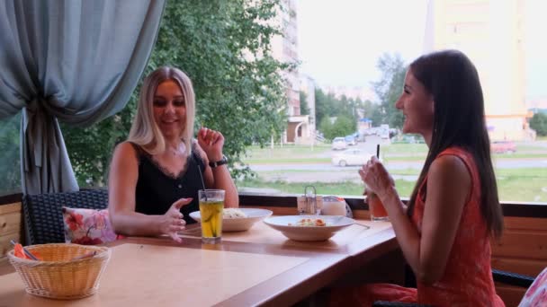Две подруги отдыхают вместе в любимом кафе и делятся новостями, рады видеть друг друга. Внутренний портрет удивительных девушек в милых платьях, пьющих коктейли и говорящих о чем-то смешном .. — стоковое видео