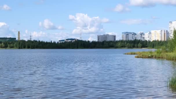 Hermoso paisaje de un pequeño lago y ciudad. Viento ligero en el lago. Las nubes se reflejan en el agua — Vídeo de stock