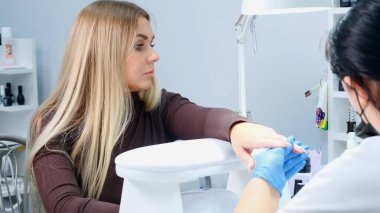 Manikürcü, güzellik salonundaki bir müşterinin tırnaklarına jel cilası sürüyor. Çivi çakın. Bıçaklı kız manikürü kaçırdı.