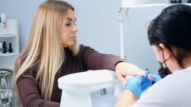 Manikürcü, güzellik salonundaki bir müşterinin tırnaklarına jel cilası sürüyor. Çivi çakın. Bıçaklı kız manikürü kaçırdı.