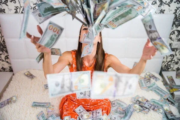Bella ragazza gode di enorme ricchezza. femmina getta un sacco di banconote su un letto bianco, getta soldi, vista dall'alto — Foto Stock