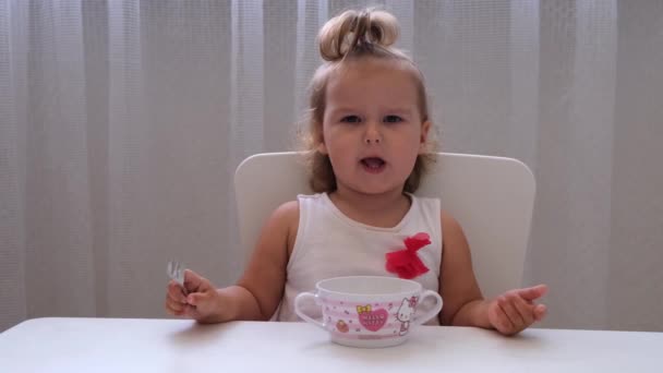 Nizhnevartovsk, Russia - August 15, 2019: Infant girl eating baby food at a small childrens table on a white background. Nutrition and feeding of children. — Stock Video