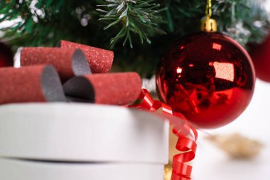 Noel ağacının üzerinde Noel arkaplanlı bir hediye kutusunun yanında asılı duran parlak kırmızı top..