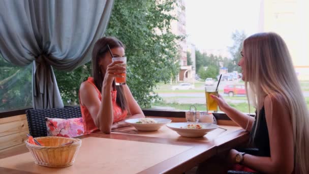 Dos amigas descansando juntas en la cafetería favorita y compartiendo noticias felices de vernos. Retrato interior de chicas increíbles en vestidos lindos bebiendo cócteles y hablando de algo divertido .. — Vídeo de stock