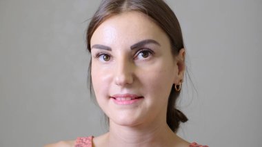 Gri bir arka plan üzerinde gülümseyen güzel beyaz bir kız portresi, kırmızı bir elbise içinde altın küpe ile.