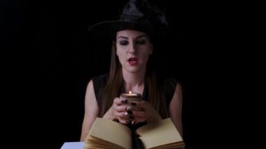 Siyah cadı kostümlü ve şapkalı güzel seksi kadın elinde bir mum tutuyor ve büyülüyor. Cadılar Bayramı partisi.