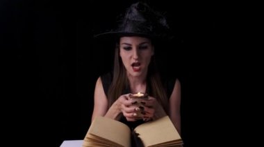 Siyah cadı kostümlü ve şapkalı güzel seksi kadın elinde bir mum tutuyor ve büyülüyor. Cadılar Bayramı partisi.