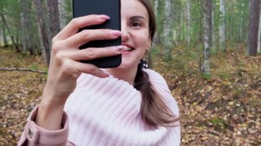 Neşeli kadın telefonda konuşuyor. Kız sonbahar ormanında selfie çekiyor..