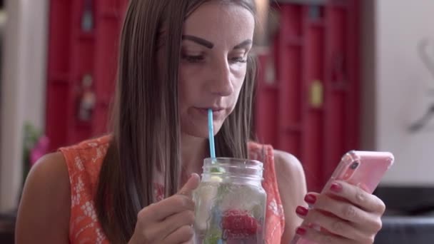 Красива жінка спілкується по телефону, розмовляє по скайпу і п'є коктейль, сидить у кафе . — стокове відео