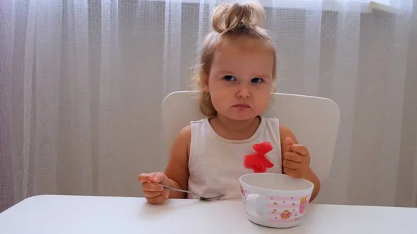 Niña comiendo comida para bebés en una mesa para niños pequeños sobre un fondo blanco. Nutrición y alimentación de los niños . — Foto de Stock