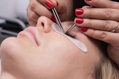 Kirpik uzatma prosedürü. Uzun takma kirpikli kadın gözü. Güzellik salonunda modadan gözün yakın çekim makro çekimi. Eller güzellik uzmanı. 