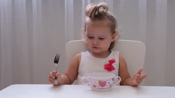 Nizhnevartovsk, Russia - August 12, 2019: Βρέφος κορίτσι τρώει παιδικές τροφές σε ένα μικρό παιδικό τραπέζι σε λευκό φόντο. Διατροφή και διατροφή των παιδιών. — Αρχείο Βίντεο