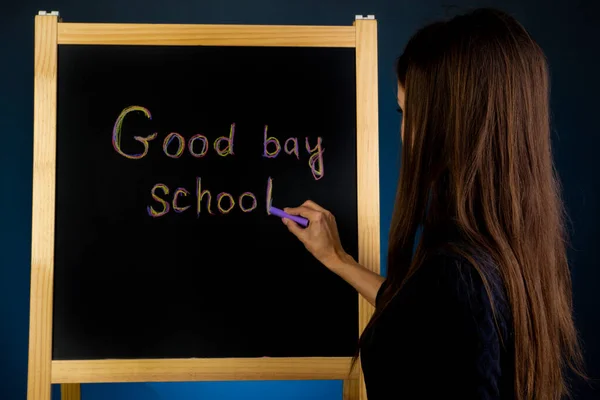 Vrouw schrijft op het zwarte krijtbord met krijt de inscriptie Vaarwel school — Stockfoto